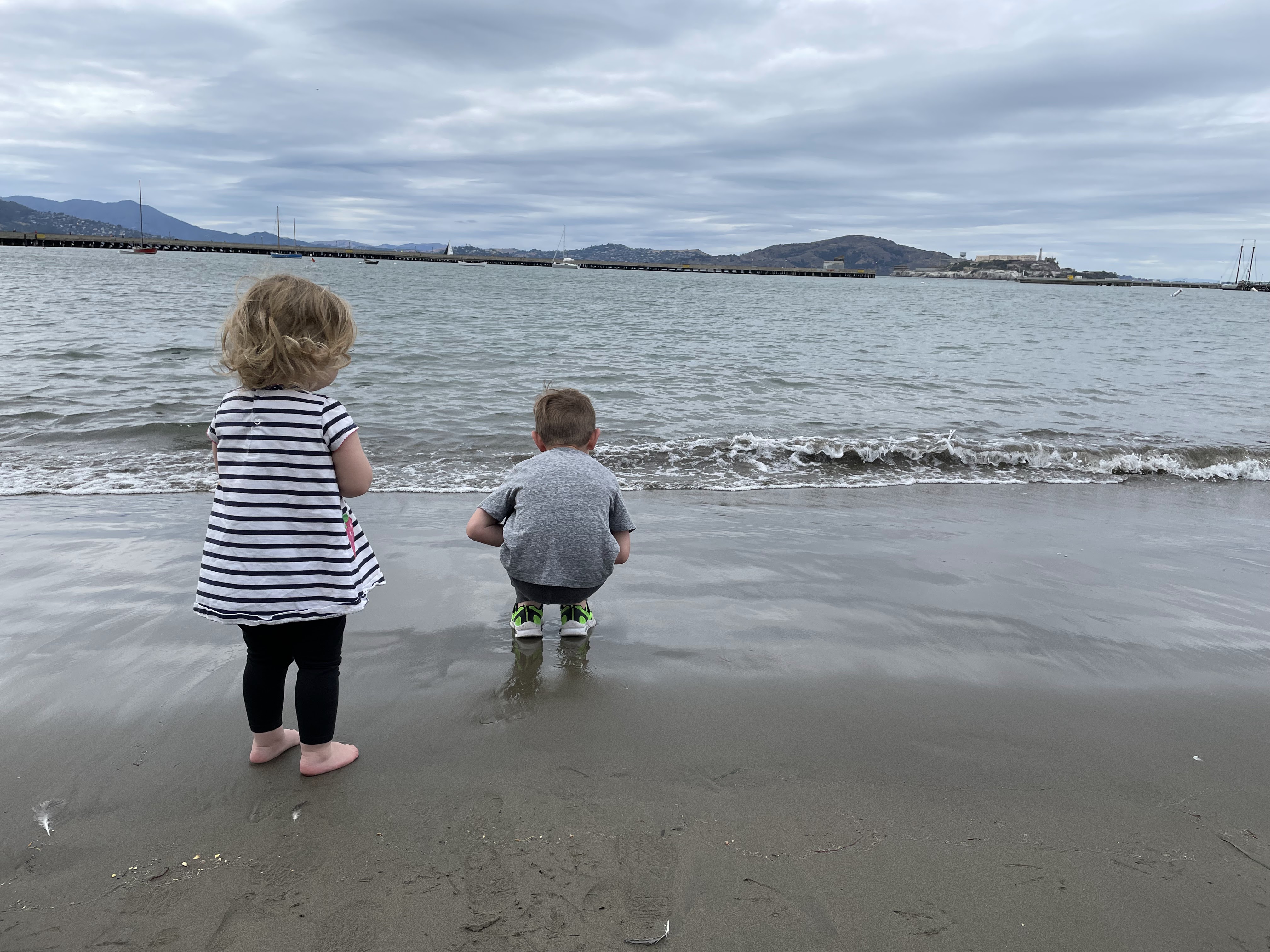 Two young children exploring the water’s edge together at a quiet shore